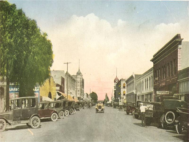 An older image of a city street lined with old-time cars