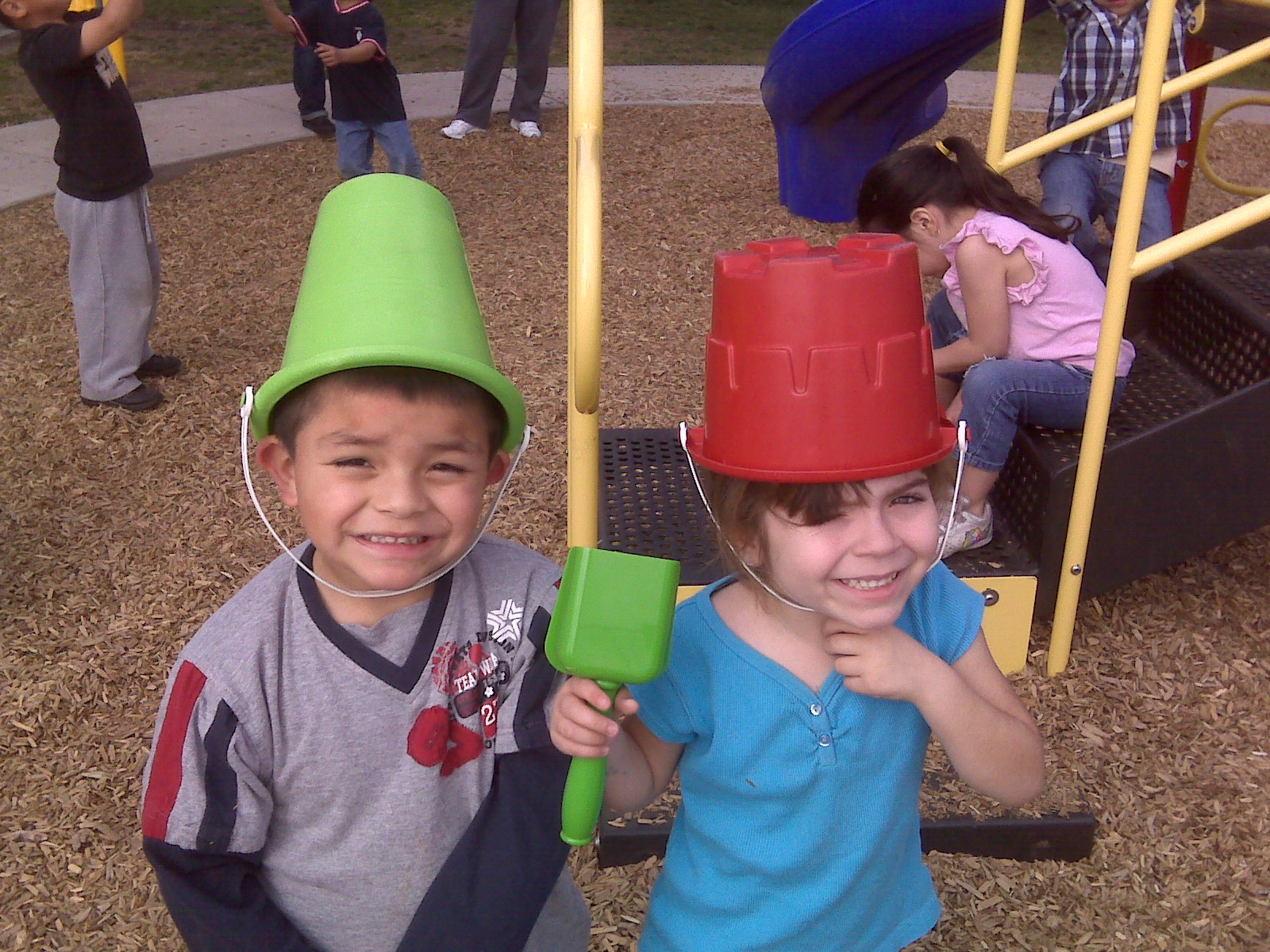 Two young children playing with buckets on their heads